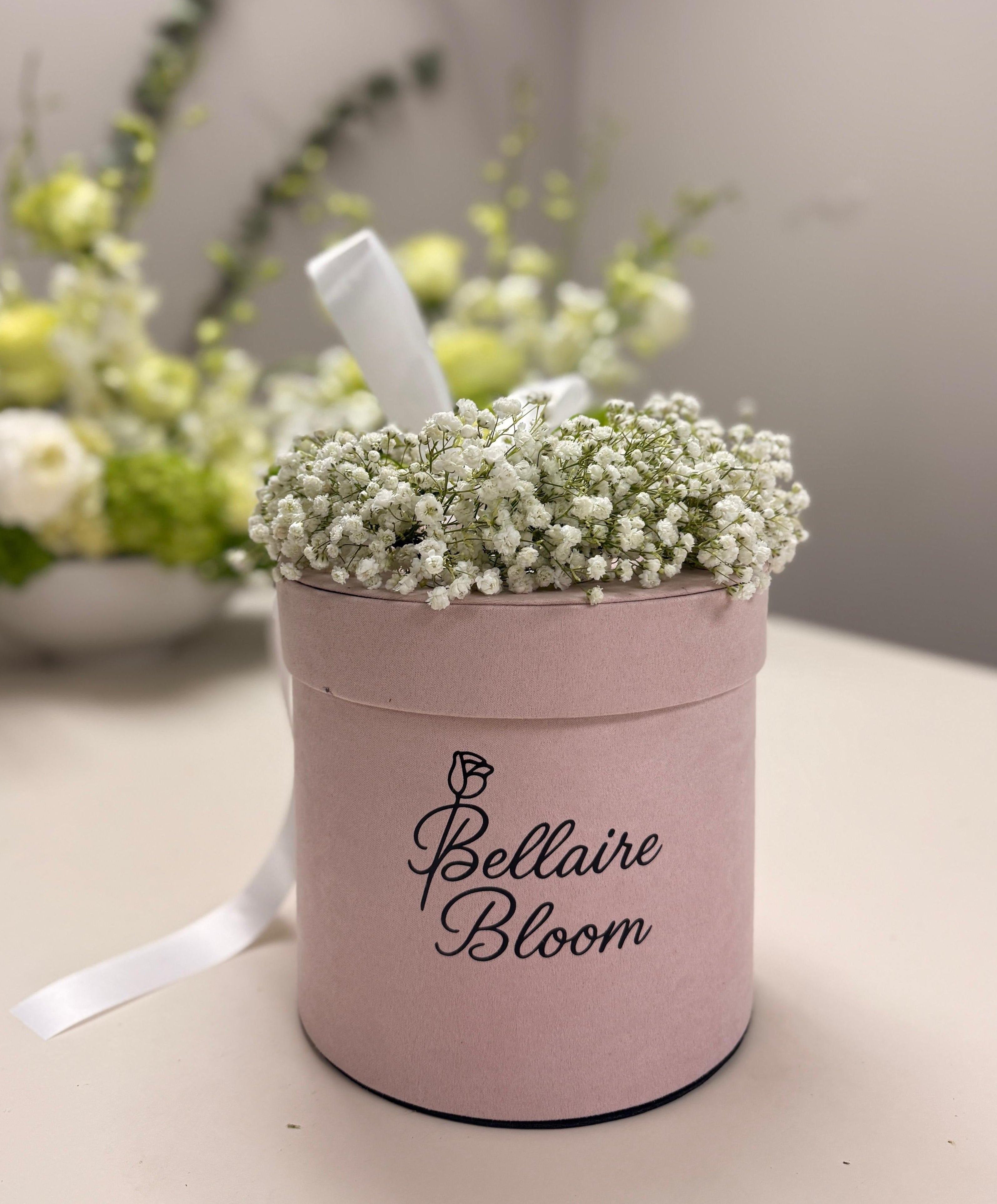 Pink flower box with baby's breath and a white ribbon, branded 'Bellaire Bloom', on a neutral background.